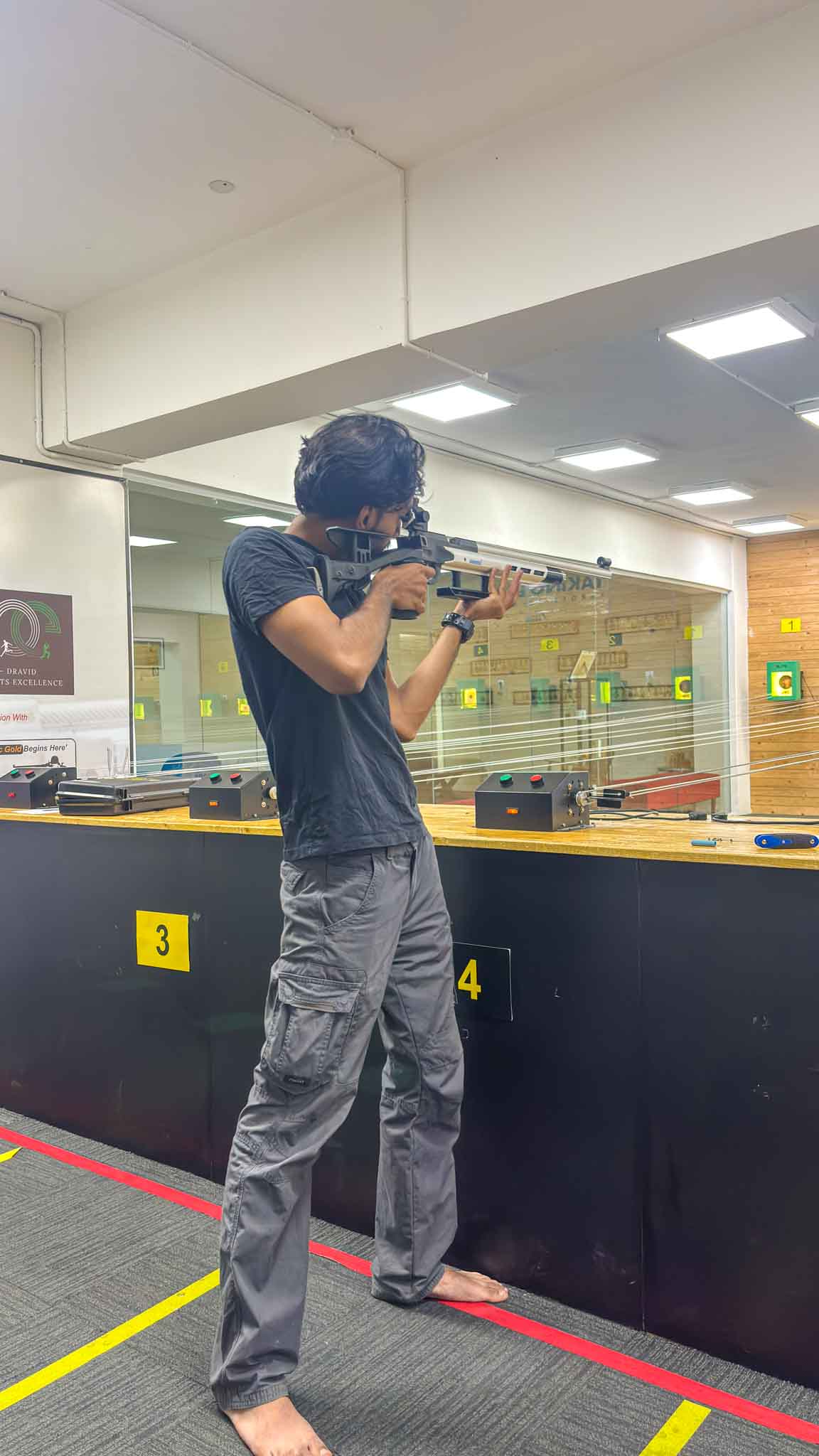 Man aiming a rifle at an indoor shooting range with shooting lanes and targets in Bengaluru.